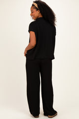 woman wearing a black short sleeve top and matching wide-leg pants, standing sideways with curly hair and a headband