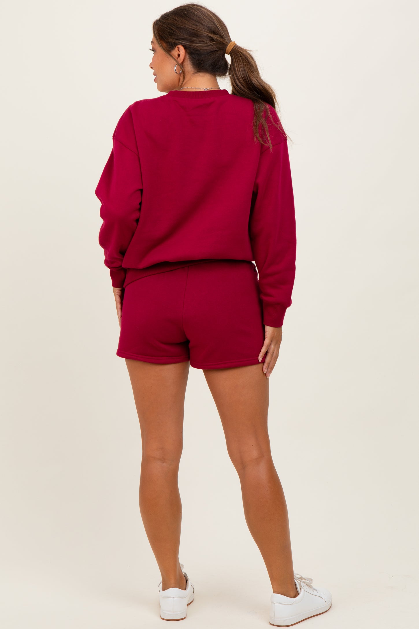 woman wearing a burgundy maternity sweatshirt and matching shorts, showing a baby bump from the back