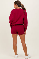 woman wearing a burgundy maternity sweatshirt and matching shorts, showing a baby bump from the back