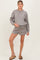 woman wearing a grey maternity sweatshirt and matching shorts, holding her baby bump while standing on a neutral background