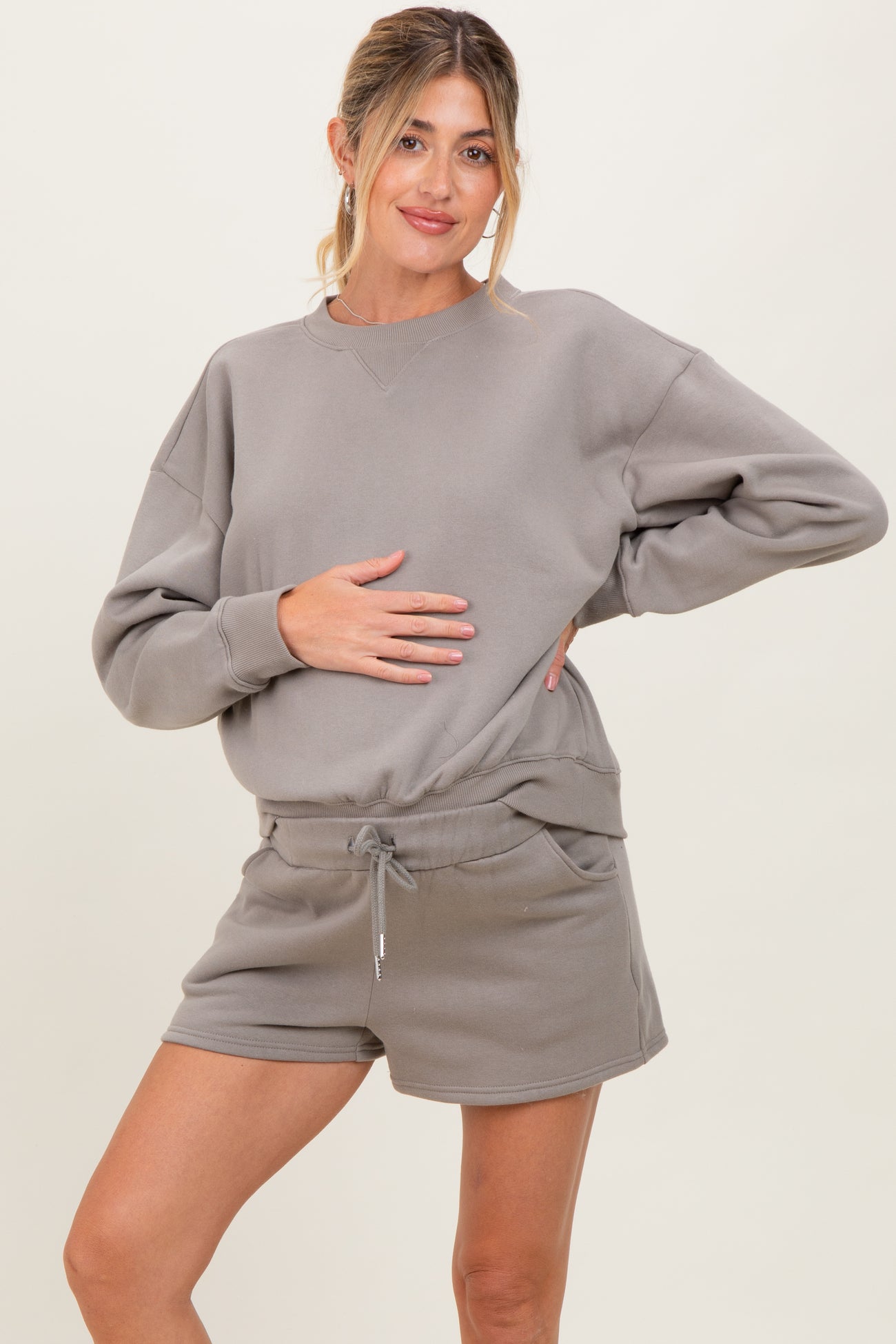 woman wearing a gray maternity sweatshirt and matching shorts, holding her baby bump