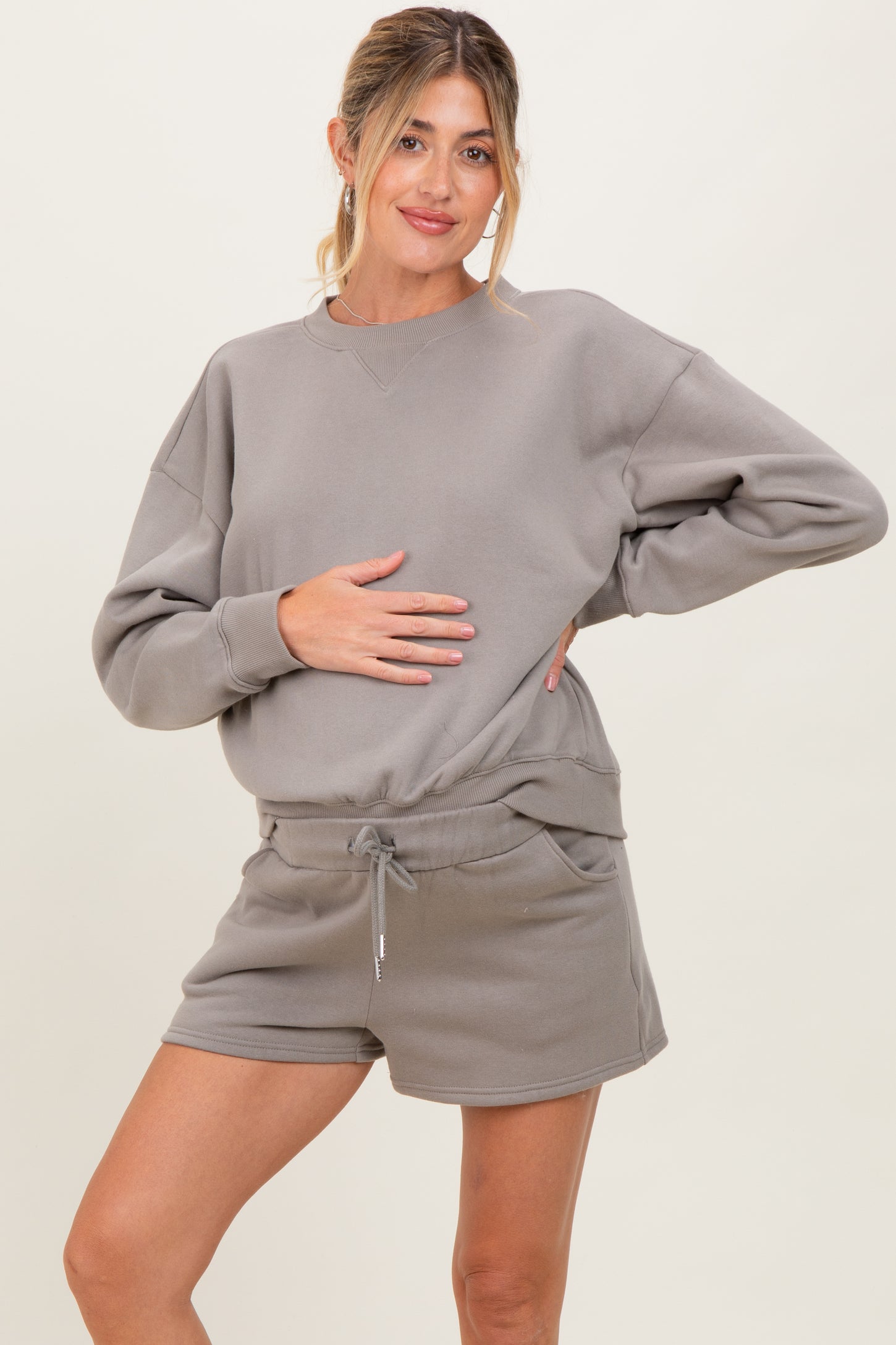 woman wearing a gray maternity sweatshirt and matching shorts, holding her baby bump