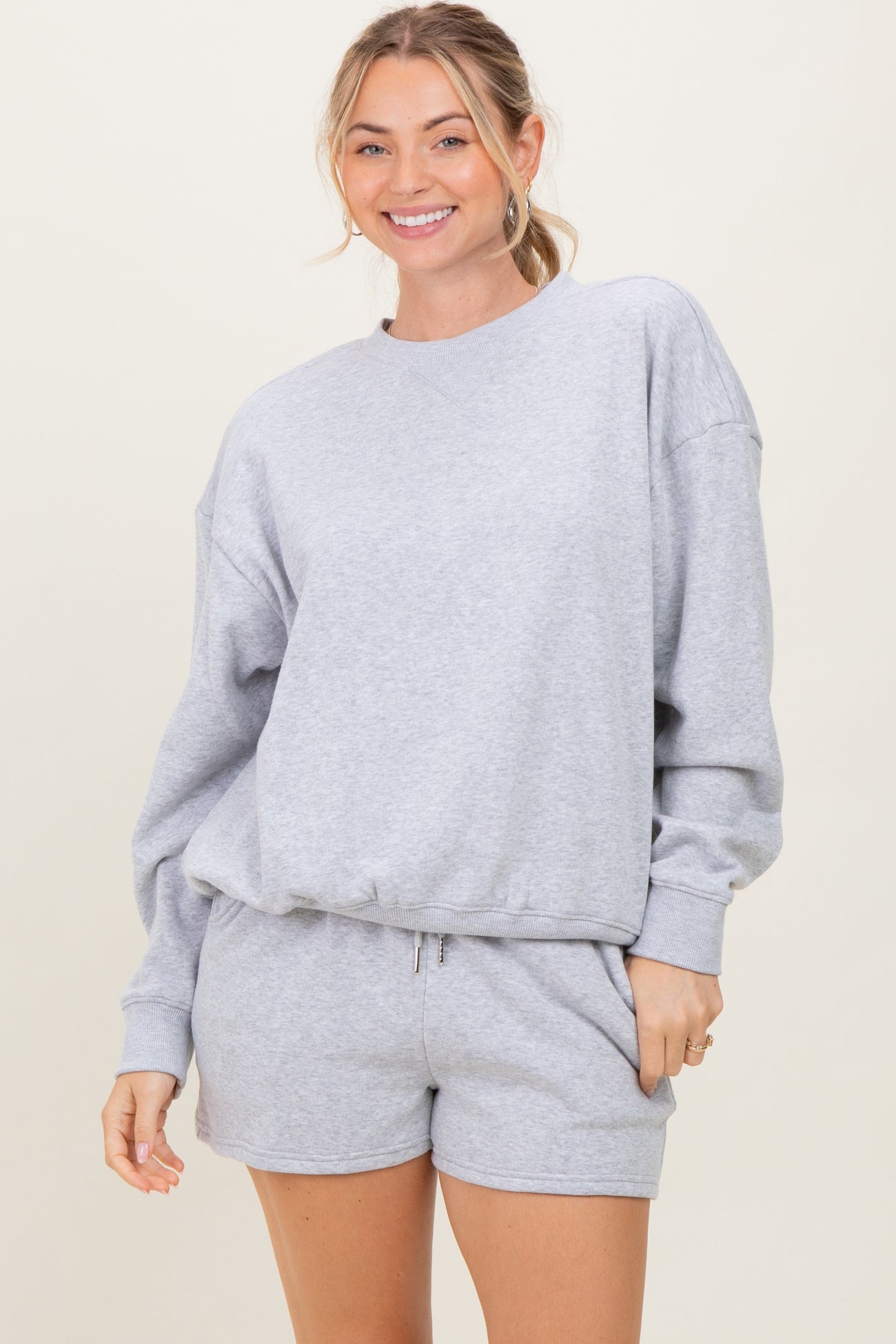 woman wearing a gray oversized sweatshirt and matching shorts, smiling at the camera