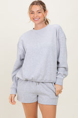 woman wearing a gray oversized sweatshirt and matching shorts, smiling at the camera