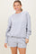 woman wearing a gray oversized sweatshirt and matching shorts, smiling at the camera