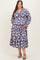 woman wearing a purple floral maternity dress with long sleeves and a tiered skirt, showing her baby bump