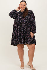 woman wearing a black floral printed plus size dress with long sleeves and a tiered skirt, standing with one hand on her hip