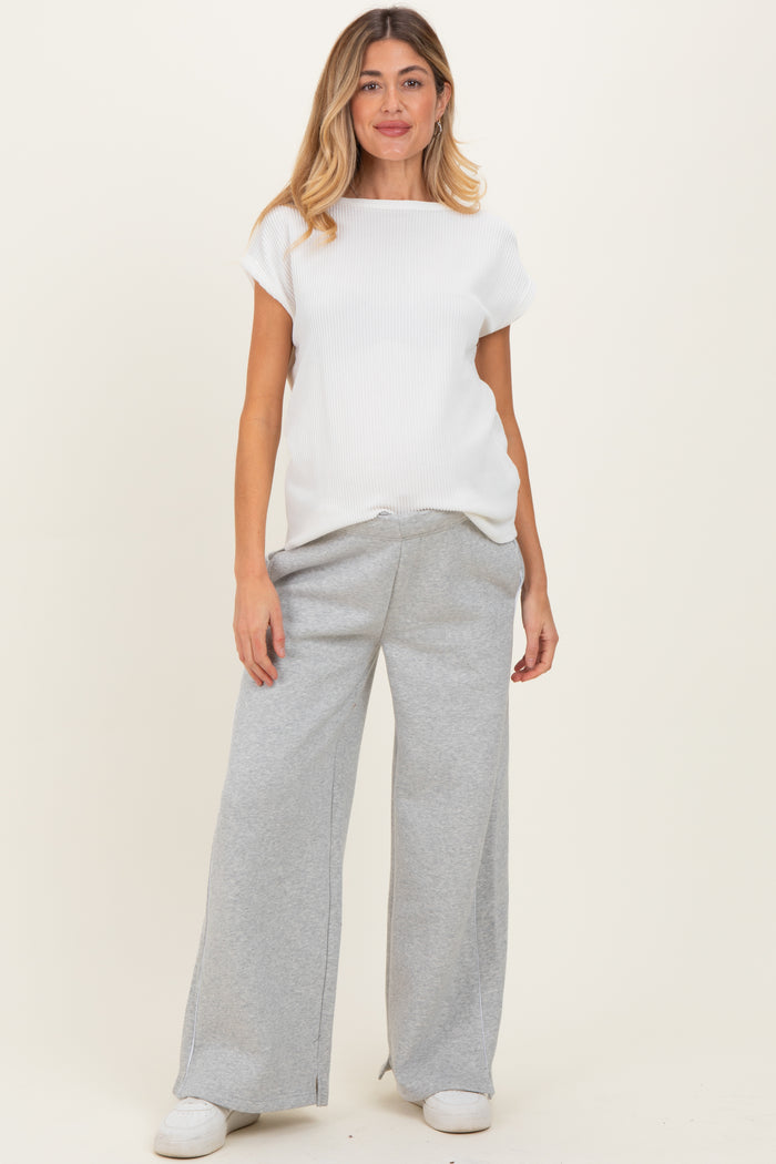 woman wearing a white ribbed maternity top and gray wide-leg sweatpants, showing her baby bump
