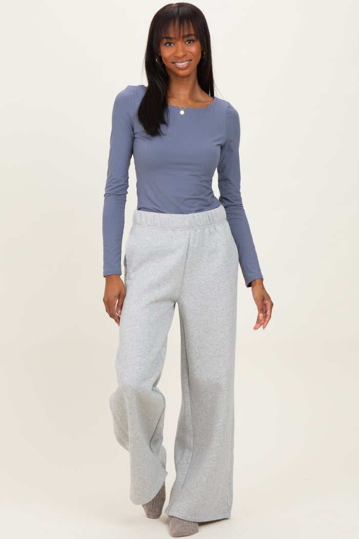 woman wearing a gray long sleeve top and light gray wide-leg sweatpants, smiling while walking toward the camera