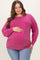 woman wearing a vibrant magenta maternity sweatshirt, gently holding her baby bump, paired with light blue jeans