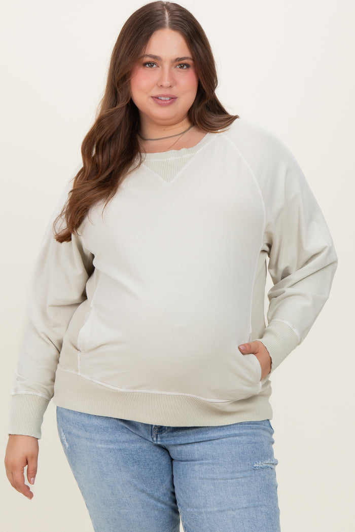 woman wearing a light beige maternity plus sweatshirt with a v-neck and side pockets, showing her baby bump
