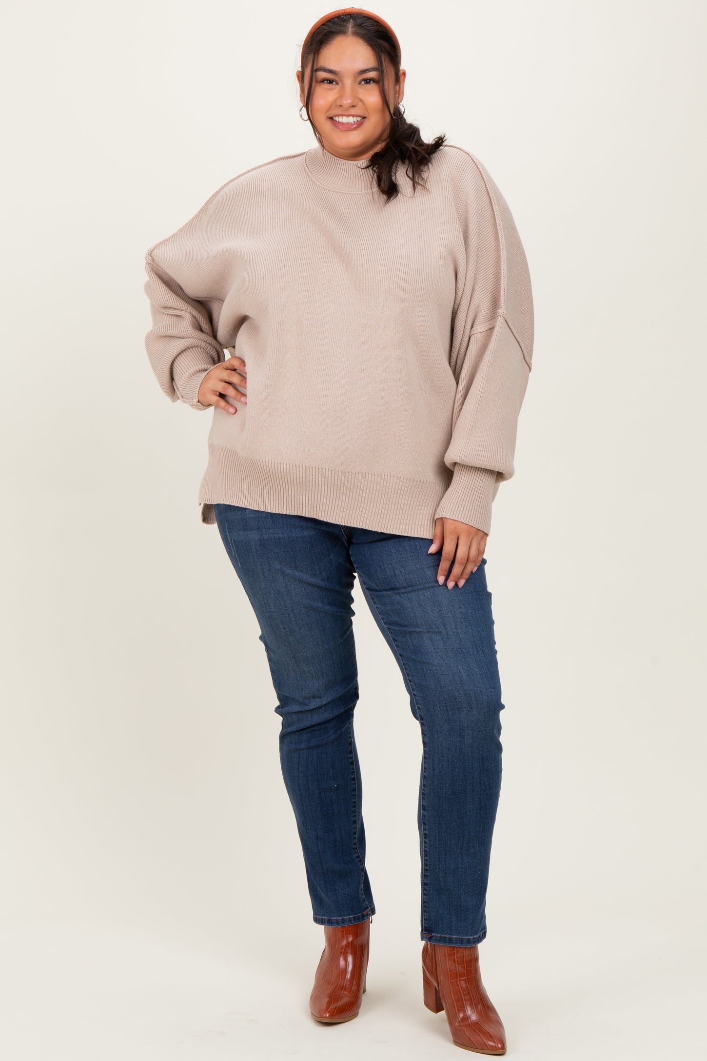 woman wearing a beige oversized sweater with long sleeves paired with blue skinny jeans and brown ankle boots
