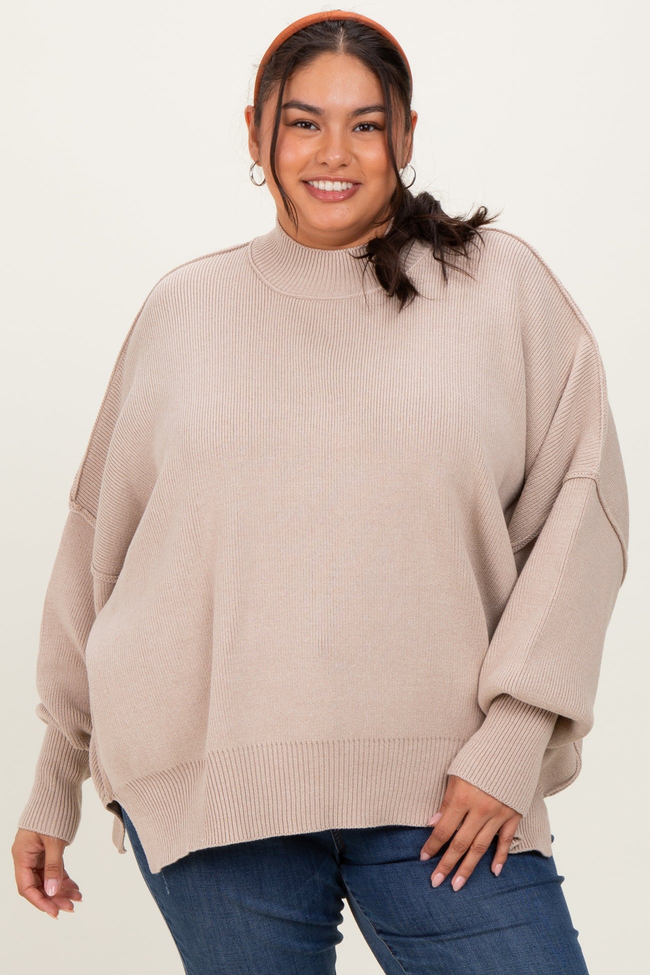 woman wearing a beige oversized sweater with a high neck and relaxed fit, paired with blue jeans
