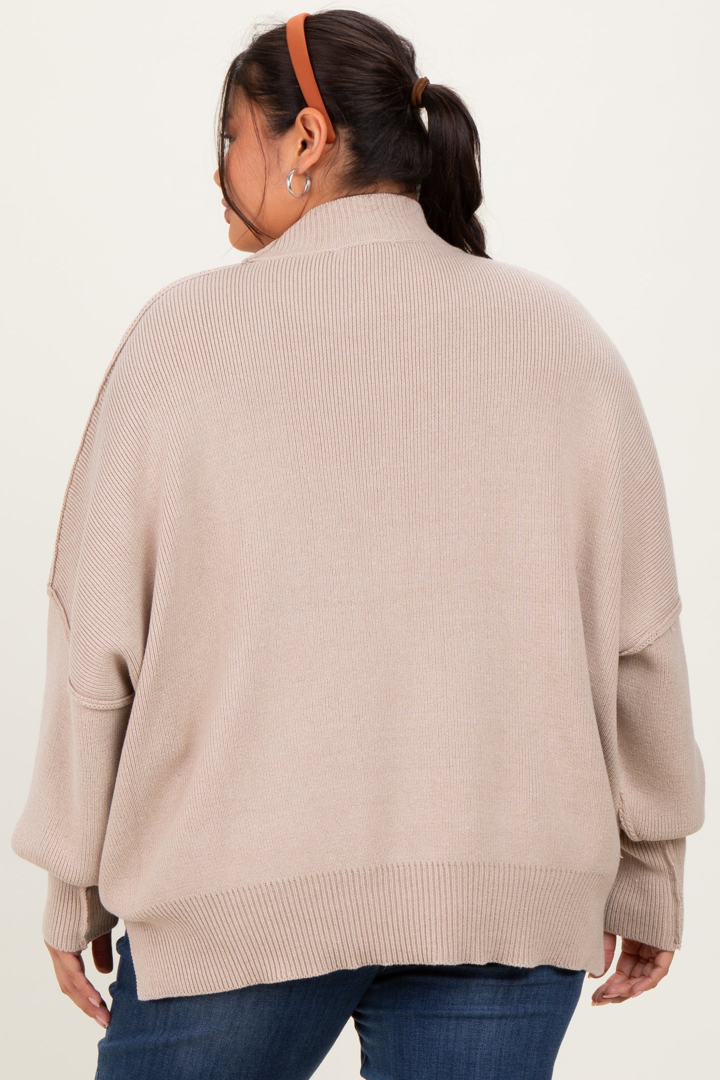 woman wearing a beige oversized sweater with batwing sleeves and a high collar, seen from the back