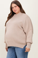 woman wearing a beige oversized maternity sweater with a high neckline and side slits, showcasing her baby bump