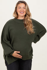 woman wearing a dark green oversized maternity sweater and holding her baby bump