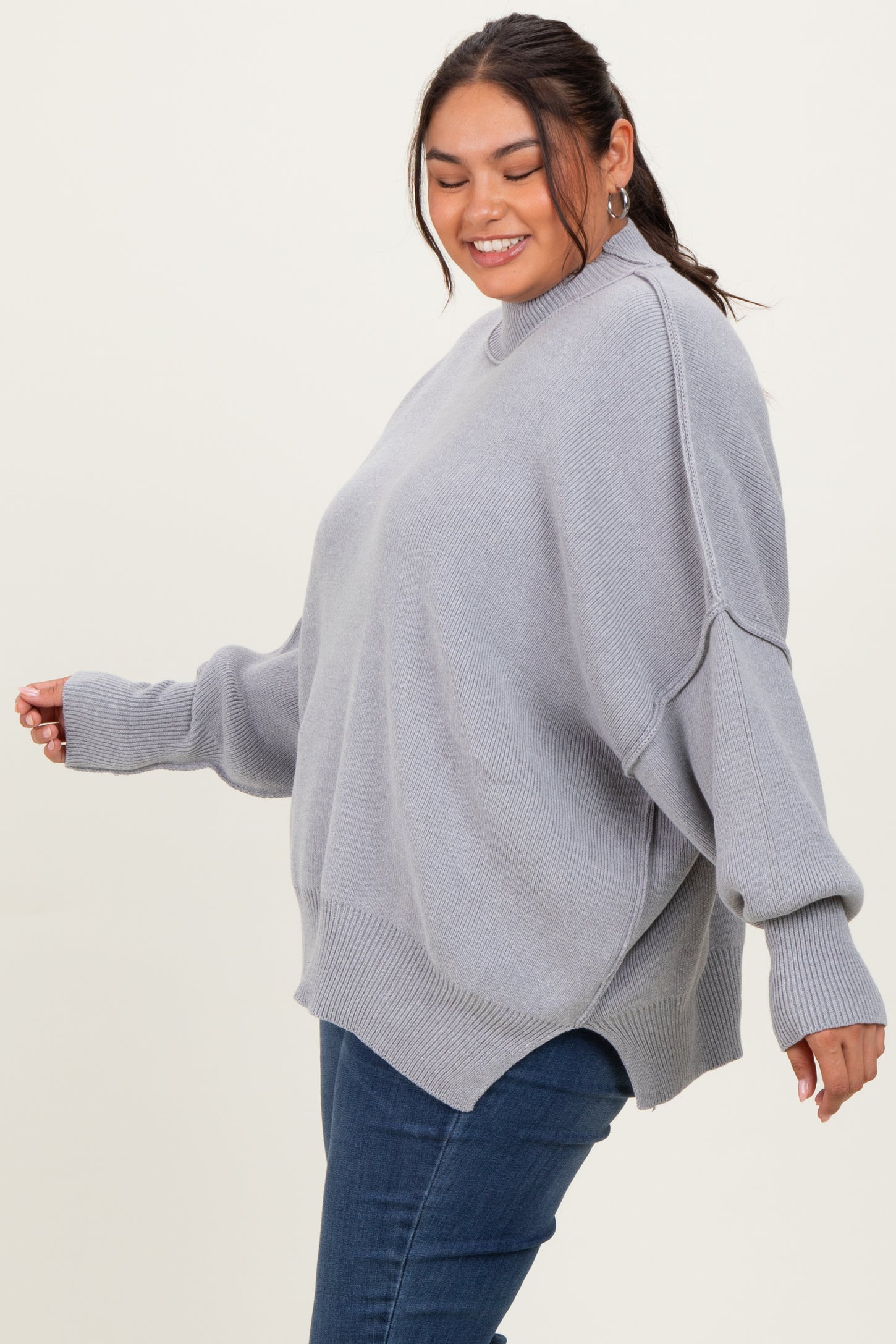 woman wearing a light gray oversized sweater with long sleeves and side slits, paired with blue jeans