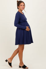 woman wearing a navy blue long sleeve maternity dress with a fitted waist and flared skirt, showing her baby bump