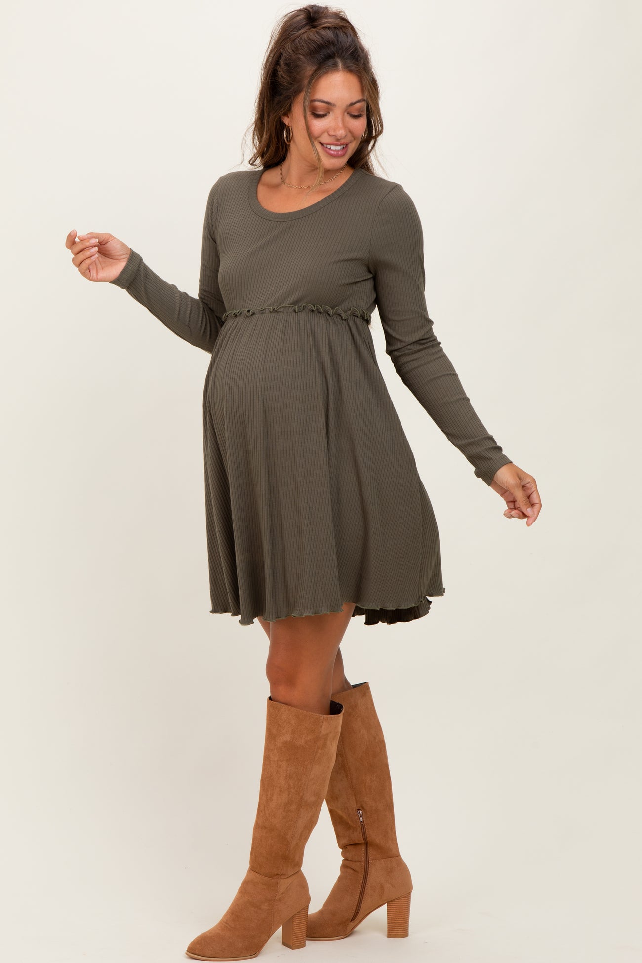 woman wearing an olive green long sleeve maternity dress with a ruffled hem and a visible baby bump