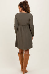 woman wearing a dark green long sleeve maternity dress with a fitted bodice and flared skirt, showing a baby bump