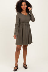 woman wearing an olive green long sleeve ribbed dress with a ruffled waist and a flared skirt