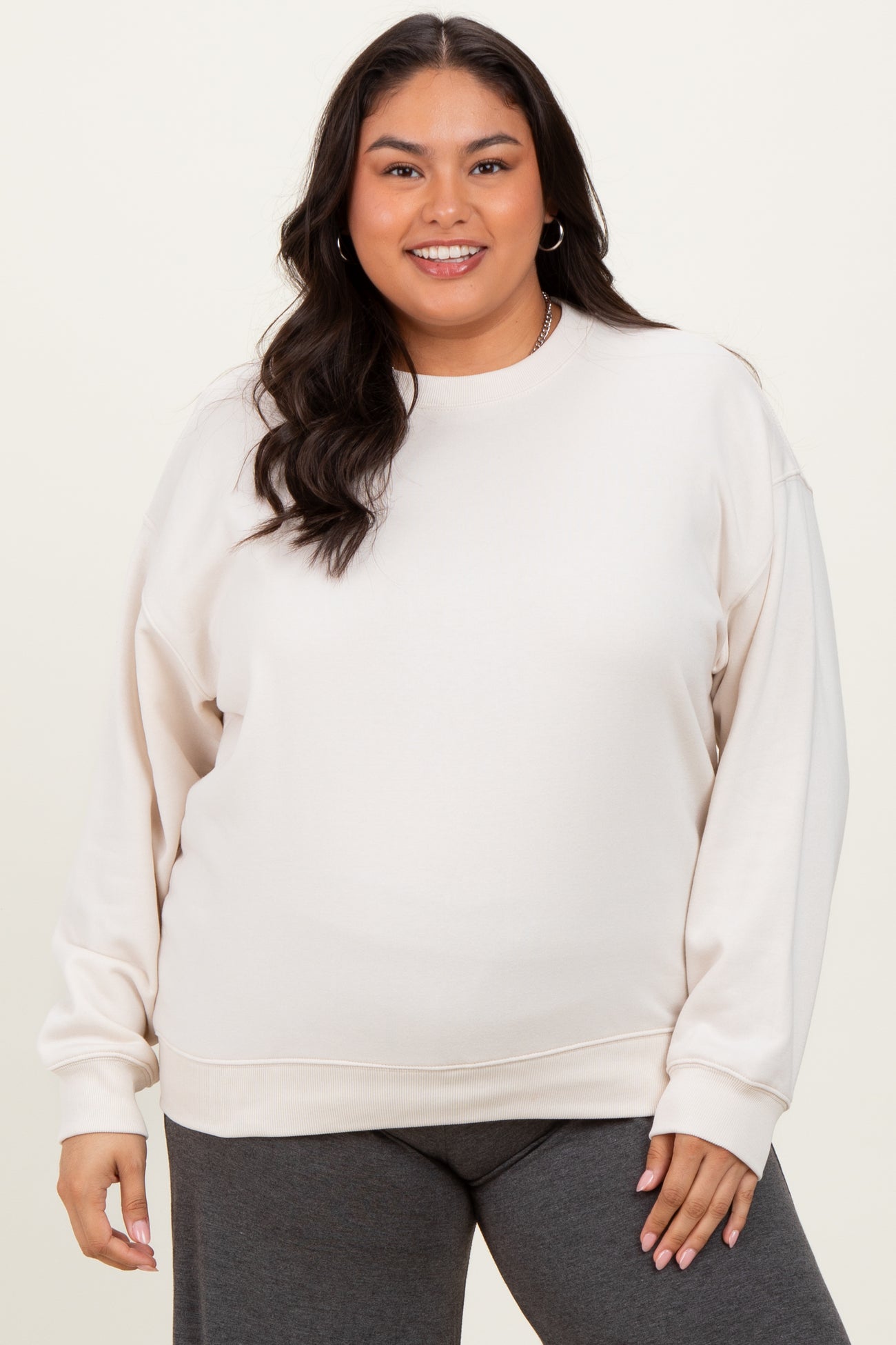 woman wearing a light beige plus size sweatshirt with long sleeves and a relaxed fit, paired with dark gray bottoms