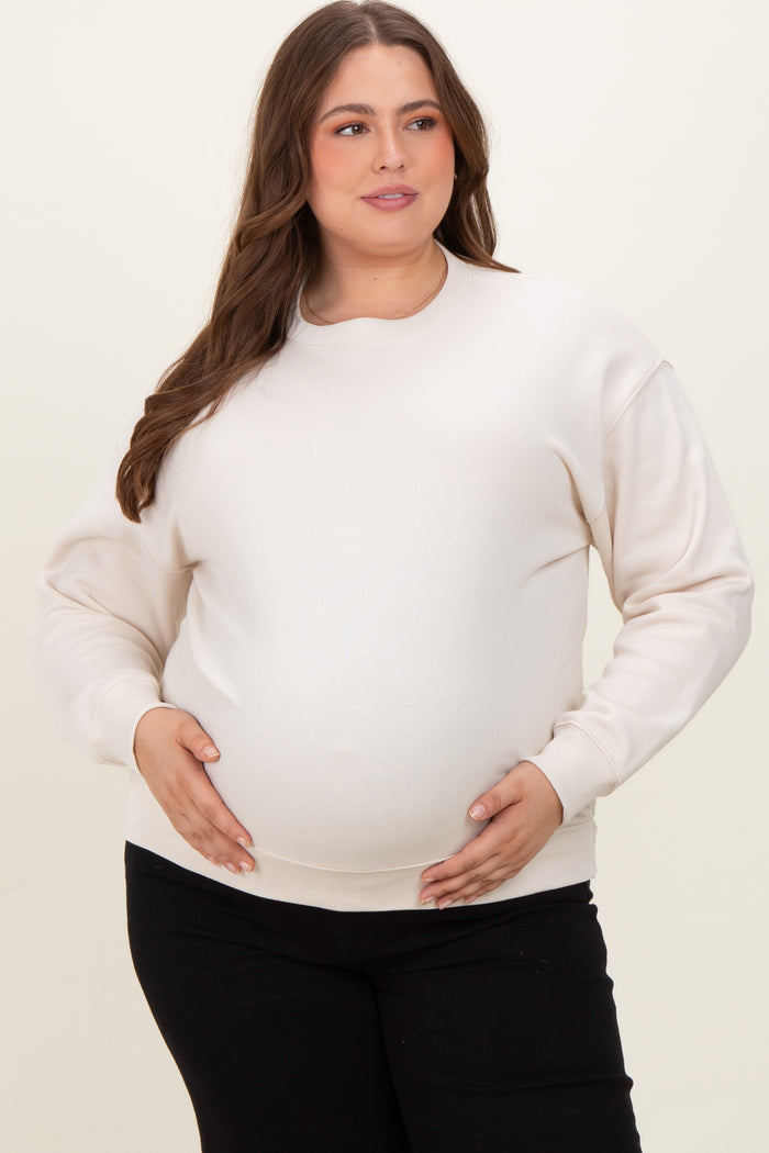 woman wearing a cream oversized maternity sweatshirt and holding her baby bump