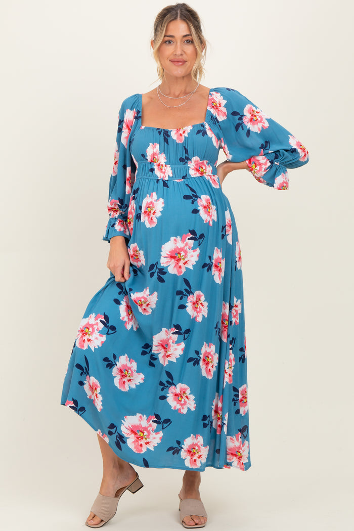 woman wearing a blue floral maternity maxi dress with long sleeves and a square neckline, showcasing her baby bump
