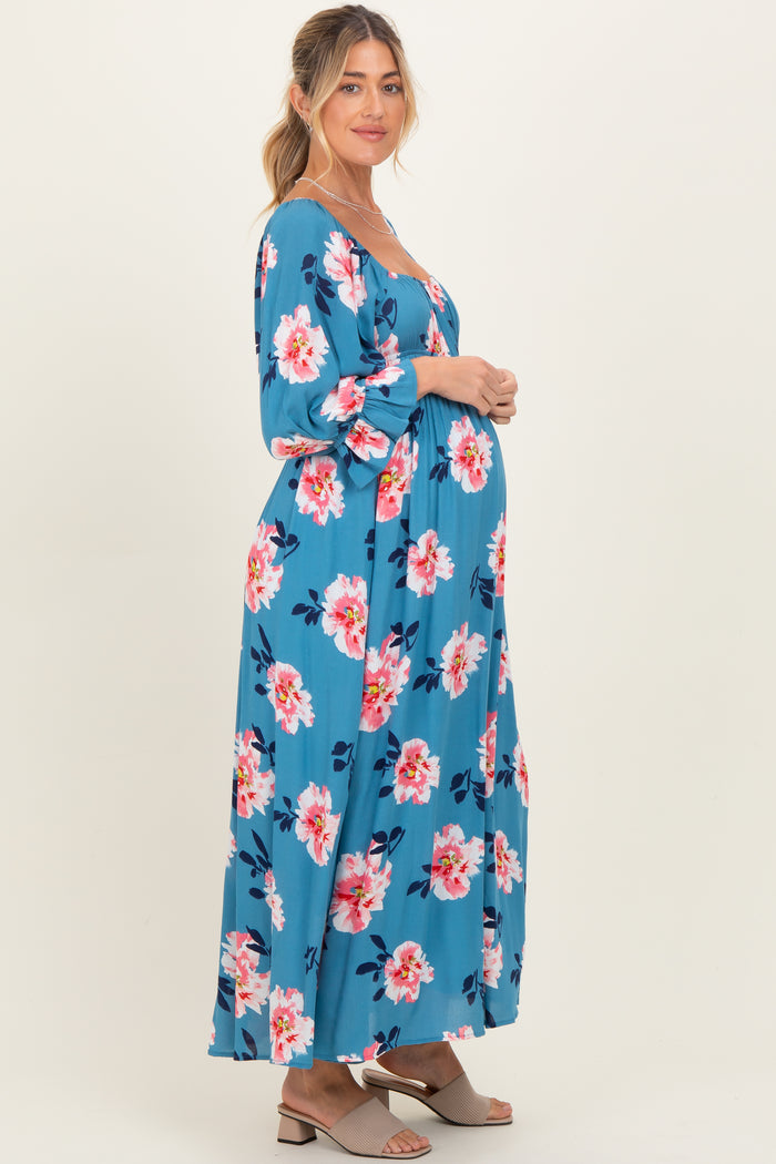 woman wearing a blue floral maternity maxi dress with long sleeves and a visible baby bump