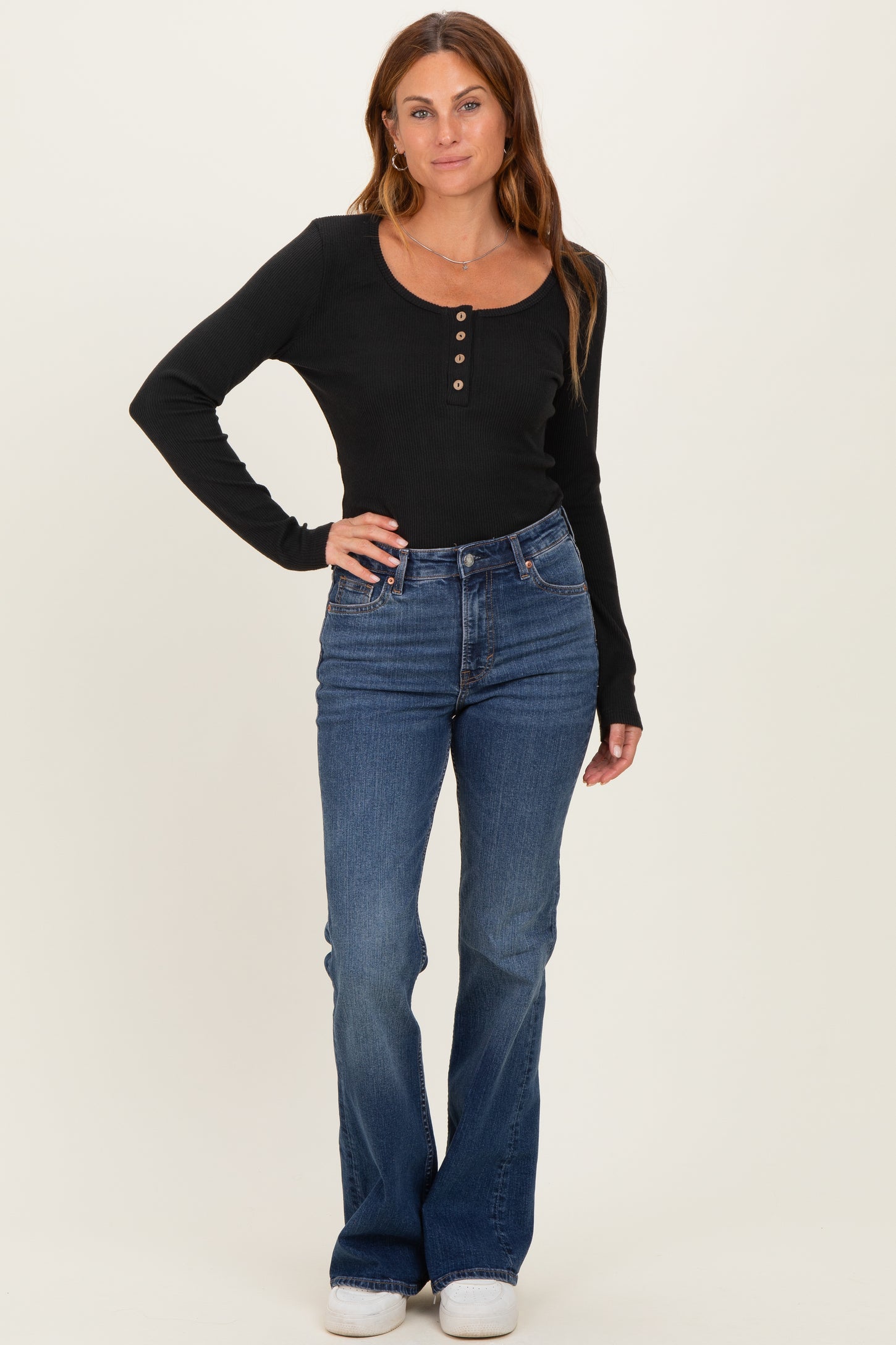 woman wearing a black long sleeve ribbed top with buttons and blue flared jeans standing upright