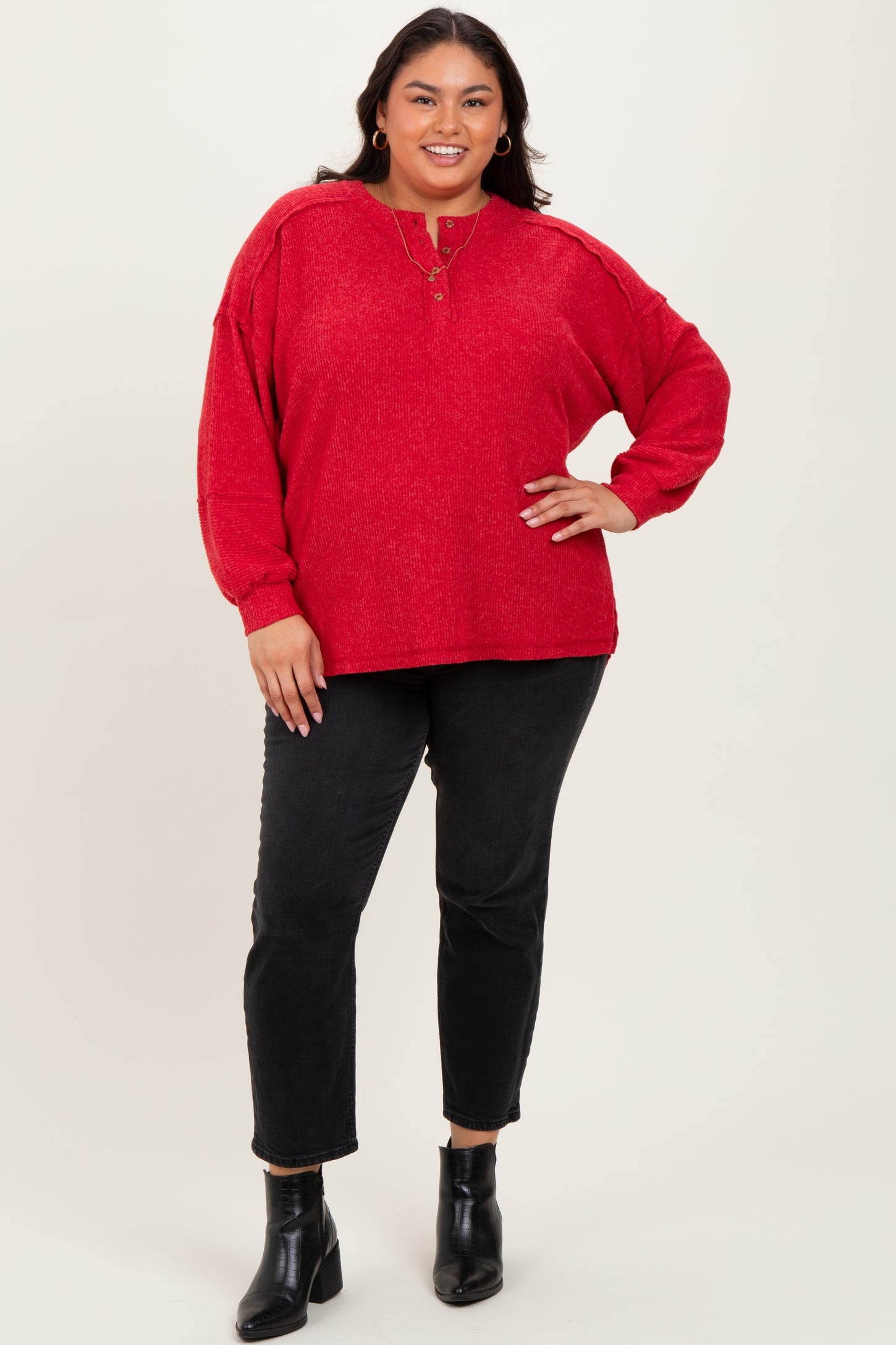 woman wearing a red oversized sweater with a button detail and black jeans, standing in black ankle boots