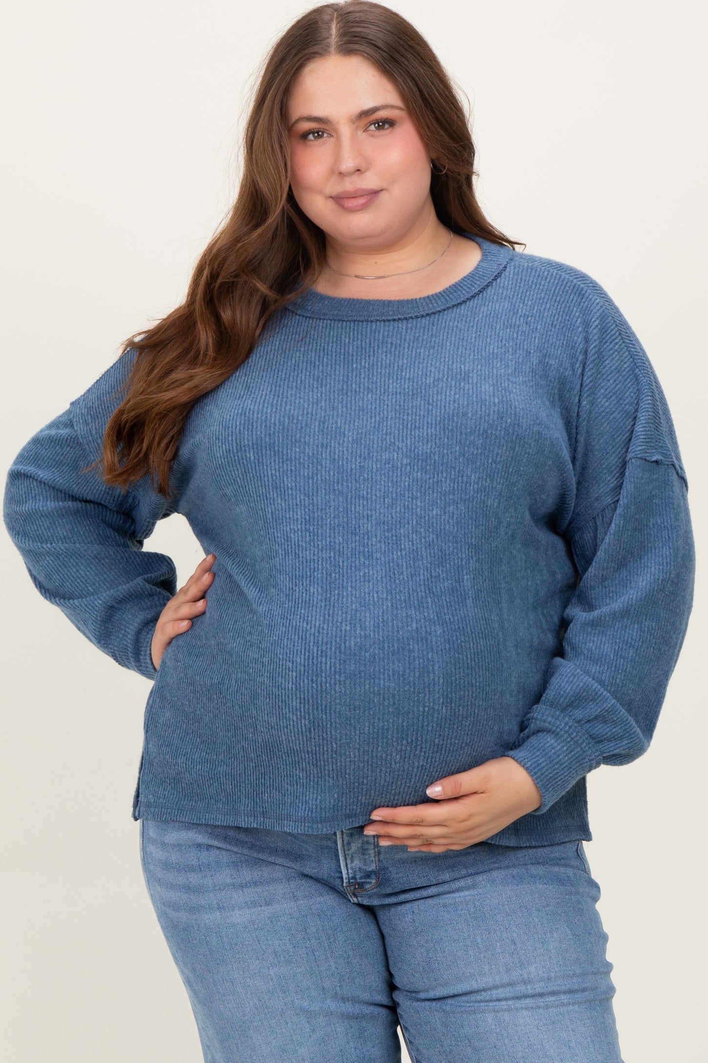 woman wearing a blue ribbed maternity sweater and holding her baby bump