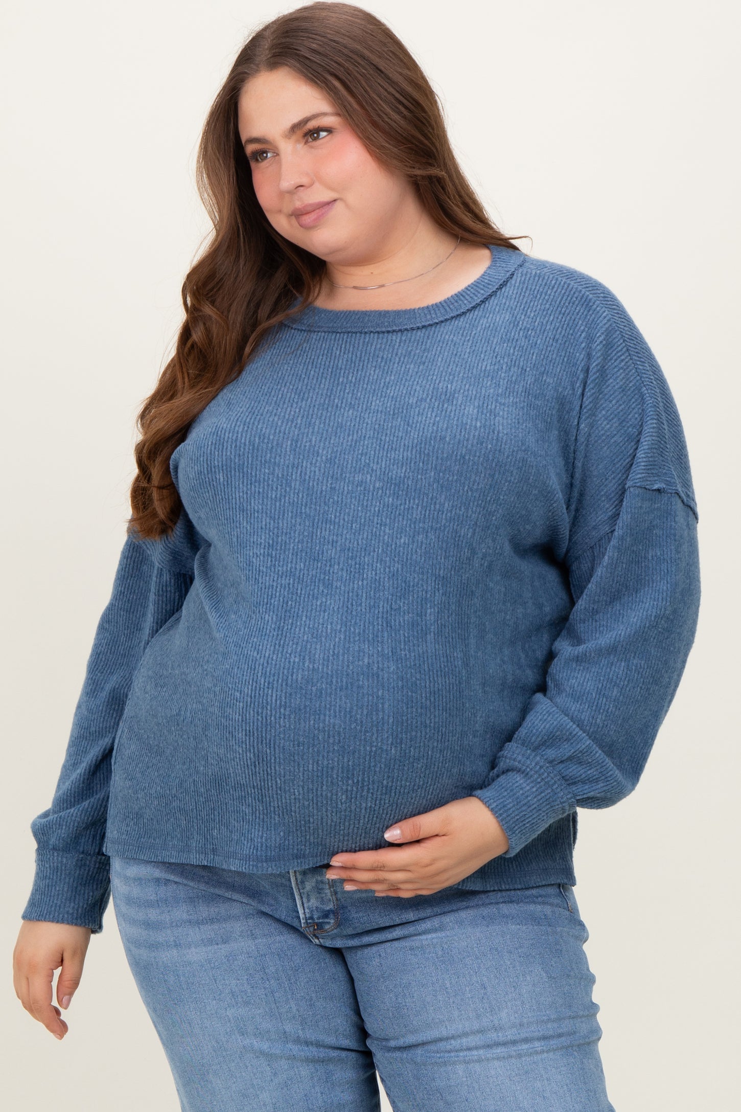 woman wearing a blue ribbed maternity sweater and holding her baby bump