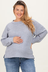 woman wearing a light gray ribbed maternity sweater, smiling and holding her baby bump, paired with blue jeans
