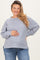 woman wearing a light gray ribbed maternity sweater, smiling and holding her baby bump, paired with blue jeans