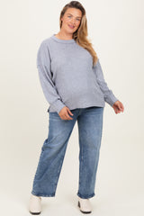 woman wearing a light gray oversized maternity sweater and blue jeans, with a visible baby bump