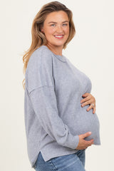 woman wearing a light gray maternity sweater, smiling and holding her baby bump, side view with relaxed fit and long sleeves