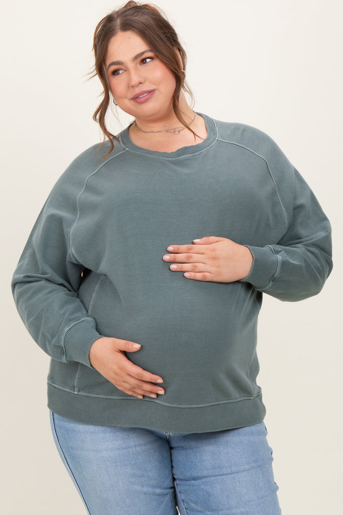 woman wearing a green oversized maternity sweatshirt and gently holding her baby bump