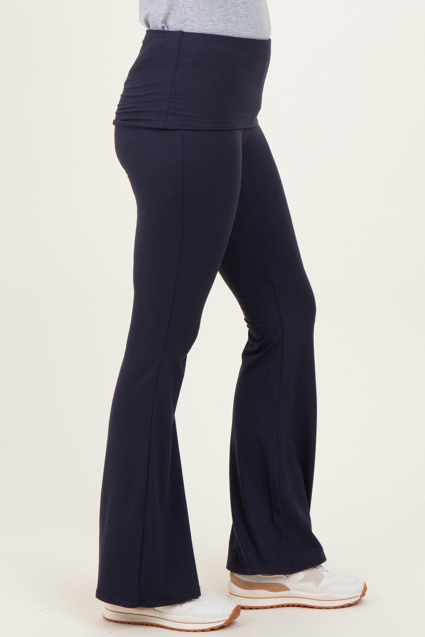 woman wearing navy blue flare yoga pants with a ruched waistband and white sneakers
