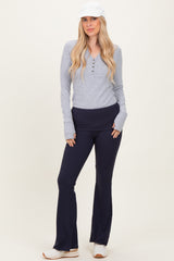 woman wearing a gray long sleeve henley top and navy flared workout pants with a white cap and sneakers