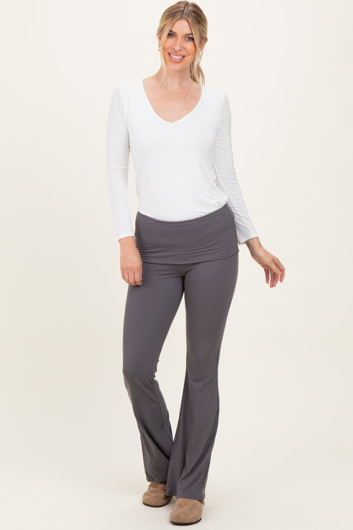 woman wearing a white long sleeve v-neck top and gray flared pants, smiling and standing against a light background