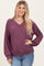 woman wearing a burgundy v-neck oversized sweater with balloon sleeves and a fitted waist, paired with light blue jeans