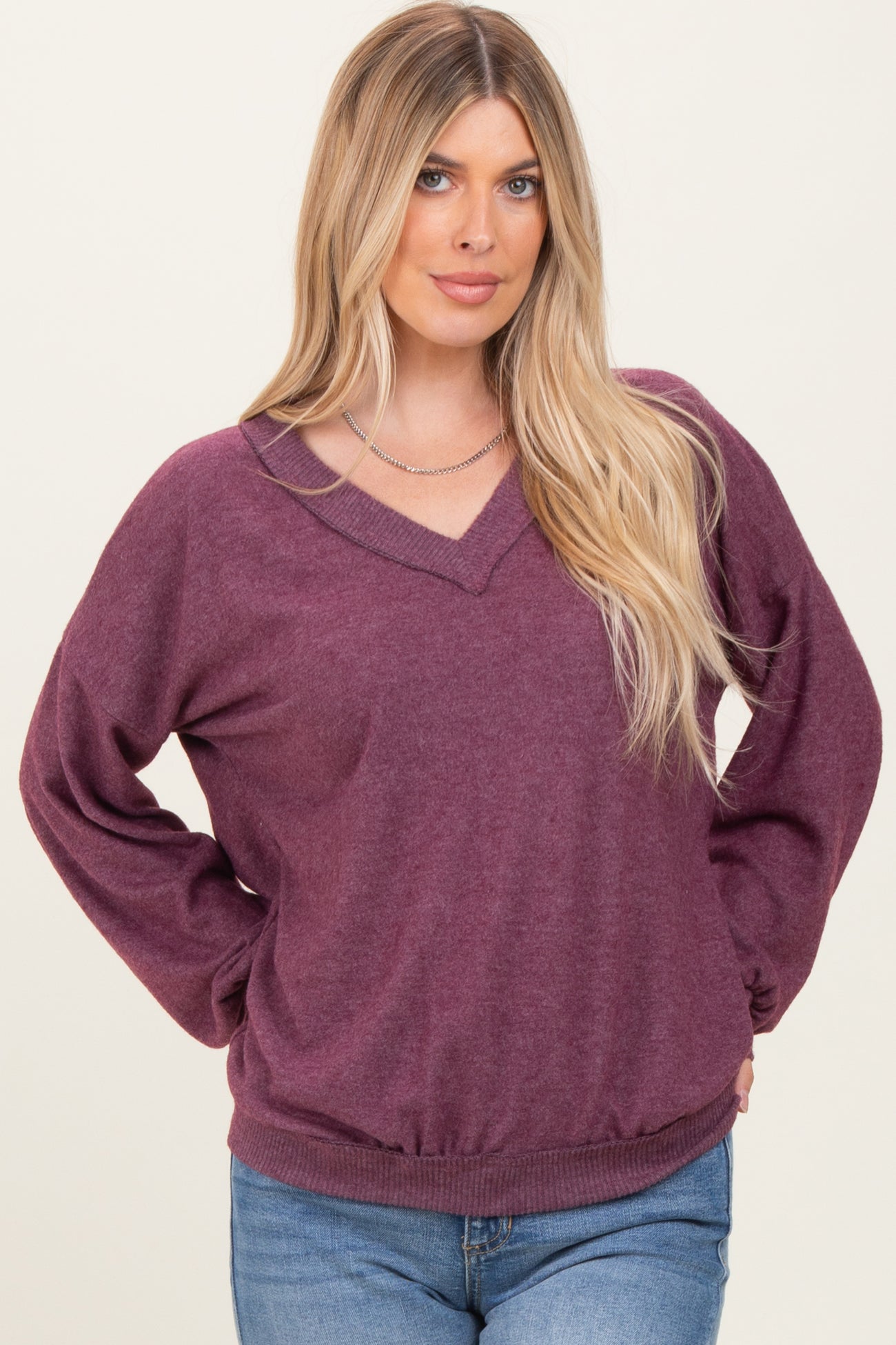 woman wearing a burgundy v-neck oversized sweater with long sleeves and a ribbed hem, paired with light blue jeans