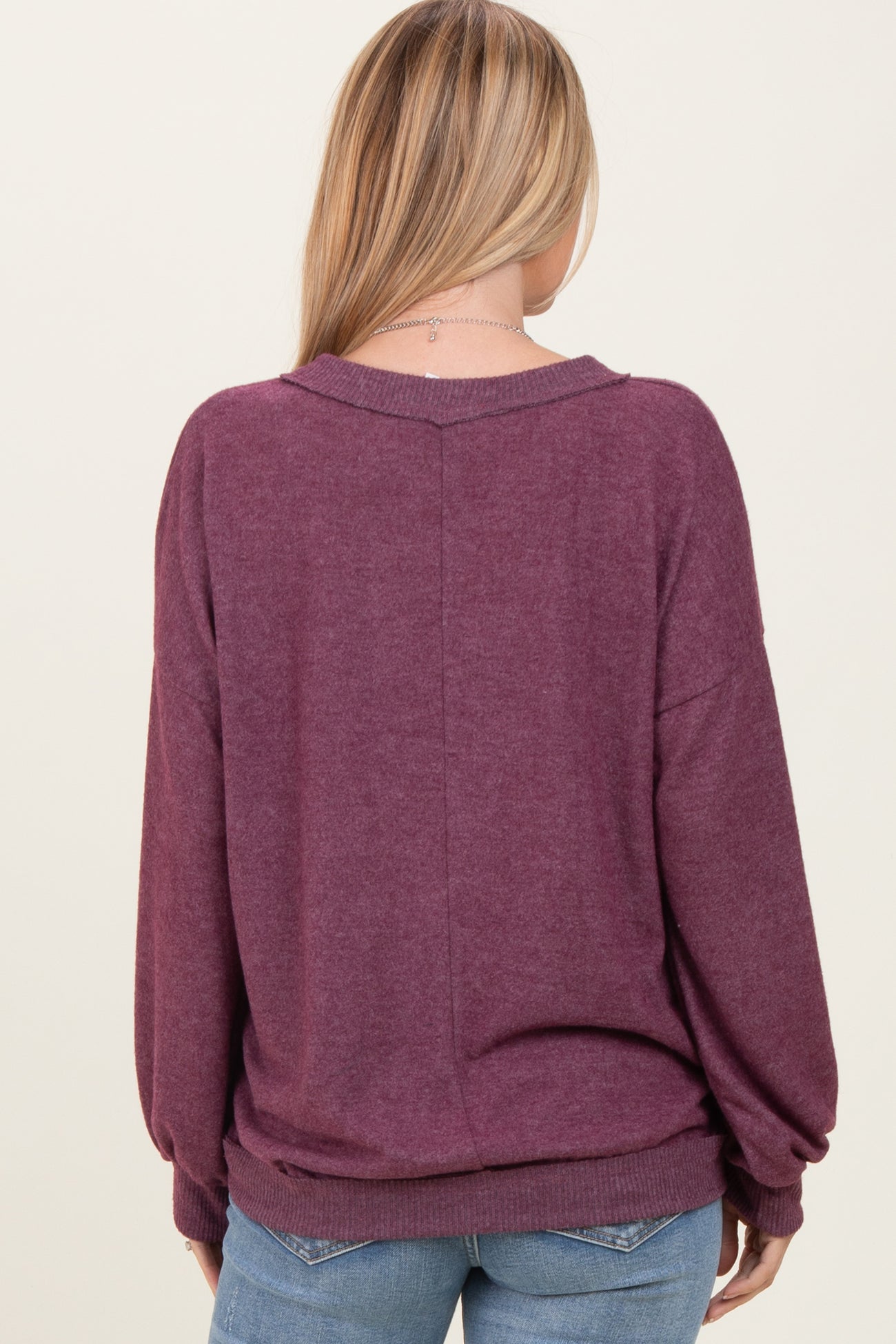 woman wearing a maroon oversized sweater with a relaxed fit, viewed from the back, paired with light blue jeans