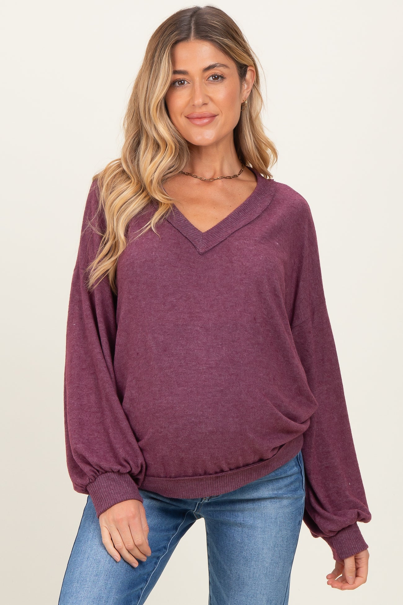 woman wearing a plum-colored maternity sweater with a v-neck and balloon sleeves, styled with blue jeans