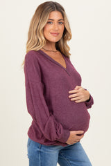 woman wearing a burgundy maternity sweater with a v-neck and balloon sleeves, cradling her baby bump