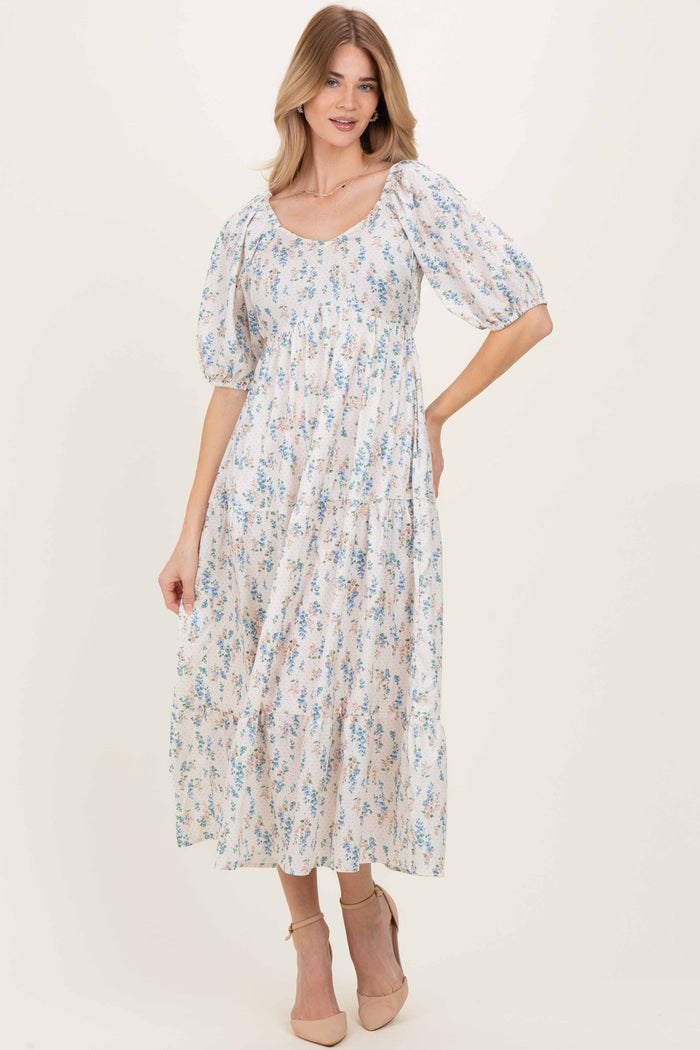 woman wearing a floral midi dress with puff sleeves and a square neckline, standing in a light background
