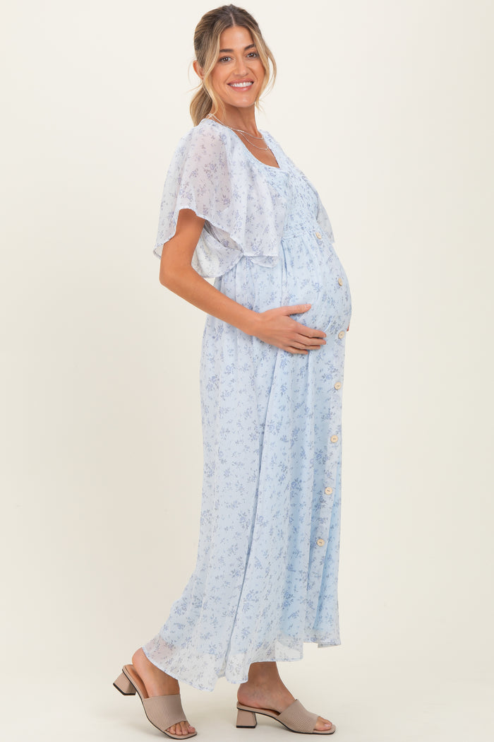 woman wearing a light blue floral maternity dress with a flowing cape sleeve and a visible baby bump