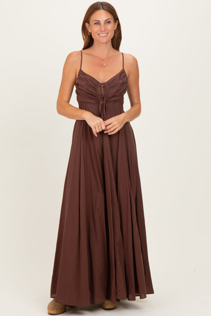 woman wearing a brown maxi dress with spaghetti straps and a cinched bodice, standing with hands clasped in front
