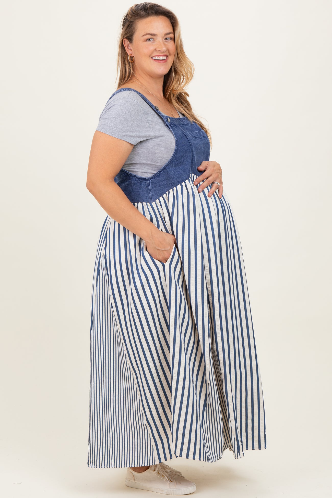 woman wearing a blue and white striped maternity plus maxi dress with pockets, showing her baby bump